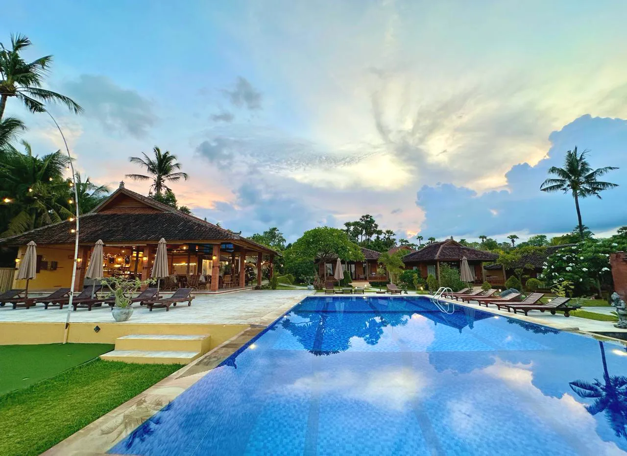 ABWonderdive resort at dusk in Kubu, Bali: the lit open-air pavilion beside an infinity pool under a pink and blue twilight sky
